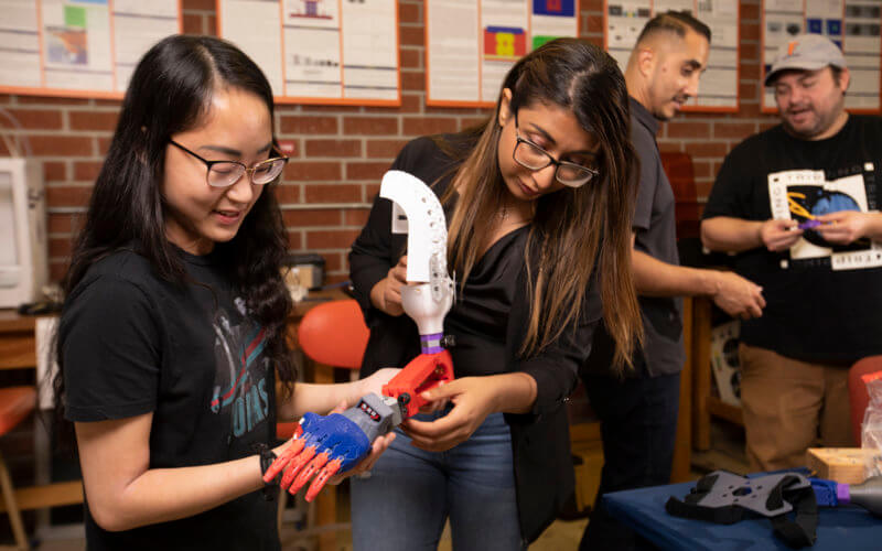 In the lab, mechanical engineering majors Aitiena Mac, left, and Marina Soliman assemble the 3D-printed prosthetic arm, while team members Miguel Garcia, left, and Kevin Mazon discuss the design.