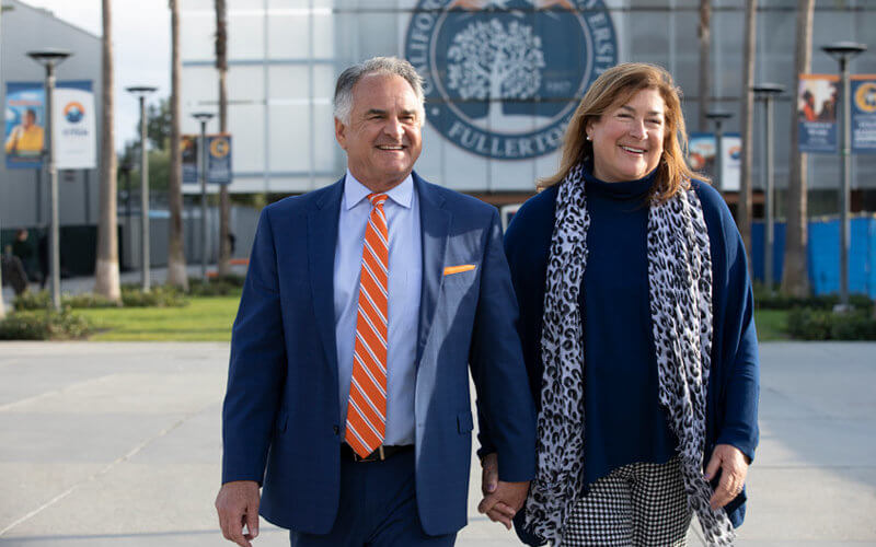 Fram and Julie Virjee holding hands while walking in front of CSUF seal