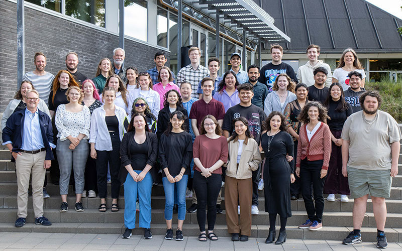 Diverse group of male and female students and faculty posing for a group photo on the steps of the University College of Northern Denmark.