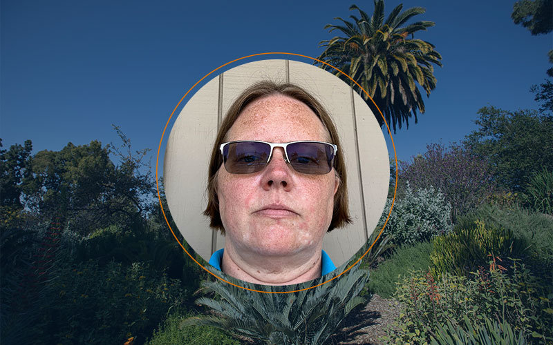 Headshot of Shannon Brown in a circular frame with a thin orange circle border. The background is a picture of Fullerton Arboretum landscape with a navy blue filter.