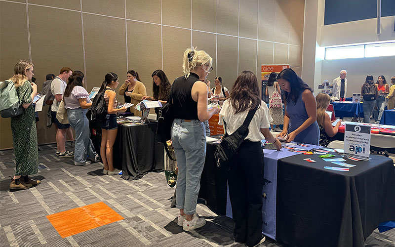 The 2022 Study Abroad Fair, which is taking place inside a Titan Student Union Pavilion. There are several students visiting various colorful tables which each have someone presenting a study abroad program.