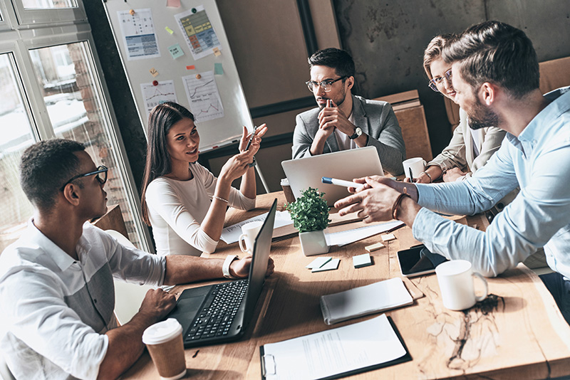 a group of people with laptops talking around a table