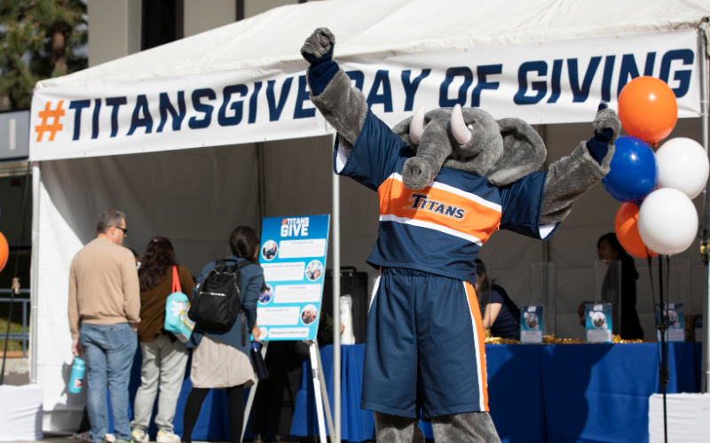 Tuffy standing in front of #TitansGive Day of Giving tent raising arms triumphantly in the air