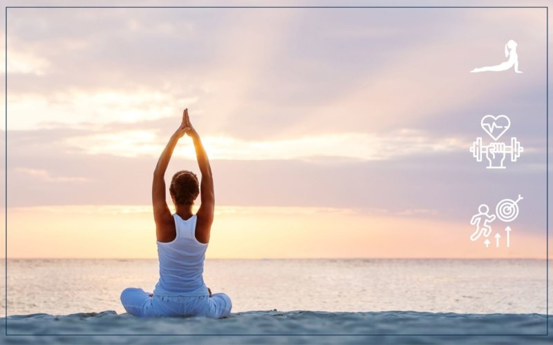 Woman sitting in yoga pose with hands overhead looking at a sunrise