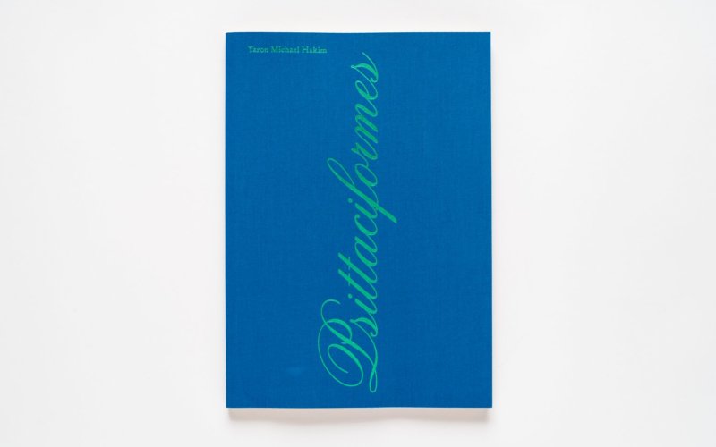 blue book cover with green foil text that reads Yaron Michael Hakim at the top left corner and the title Psittaciformes in cursive text that reads vertically from the bottom center of the cover to the top.