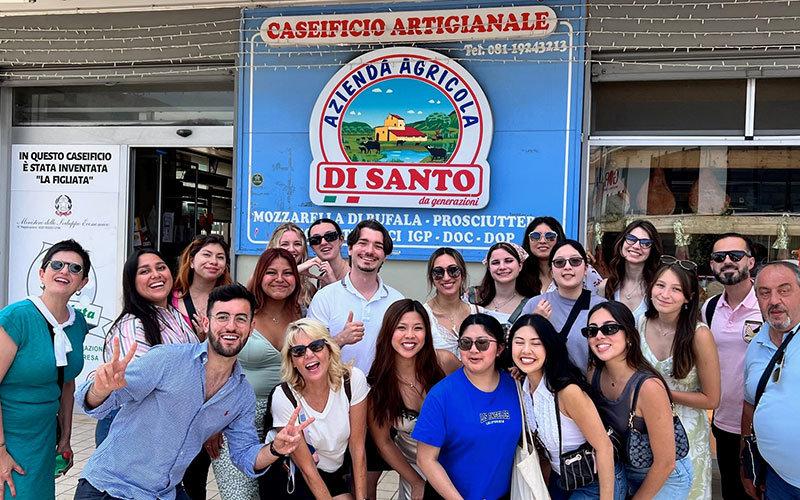 Group photo from the Summer 2023 Public Health Study Abroad Program in Italy. Diverse group of students standing outside Caseificio Di Santo.