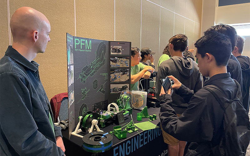 High school student observing a display of a PET Filament Machine at the Expo.
