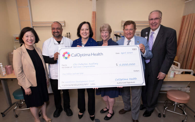Cal State Fullerton and CalOptima Health leaders stand in a simulation lab holding a large $5 million check meant for the CSUF nursing program.