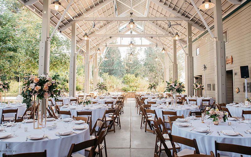 Bacon Pavilion at the Arboretum decorated for a wedding reception with white cloth tables, dark wood folding chairs, and roses.