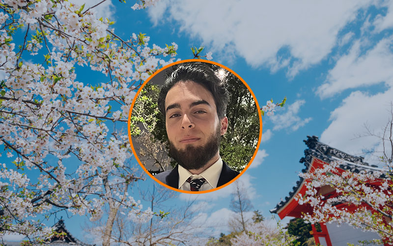 Headshot of Kyle McCaghren in a circular, orange-outlined frame. The background is a picture of cherry blossoms and a temple in Okayama, Japan.