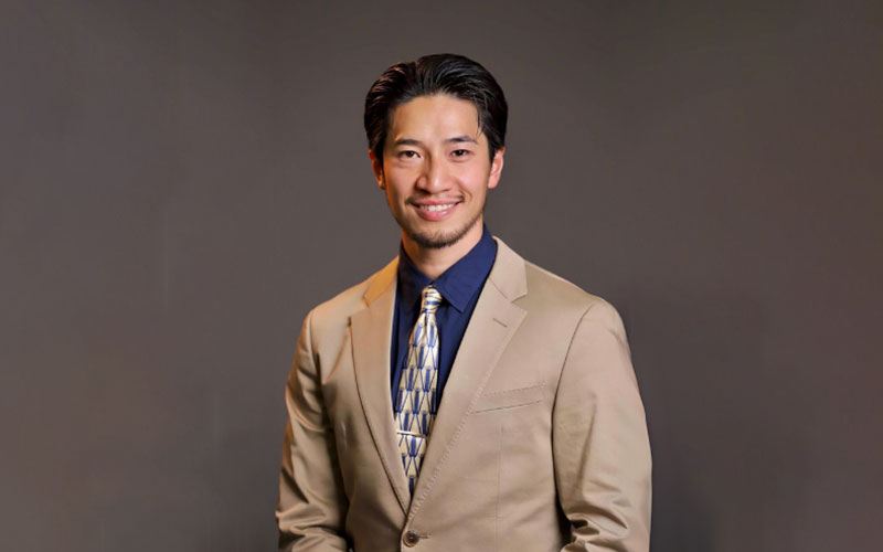 Professional headshot of Ryutaro Ichihara in business-formal attire with a dark brown backdrop.