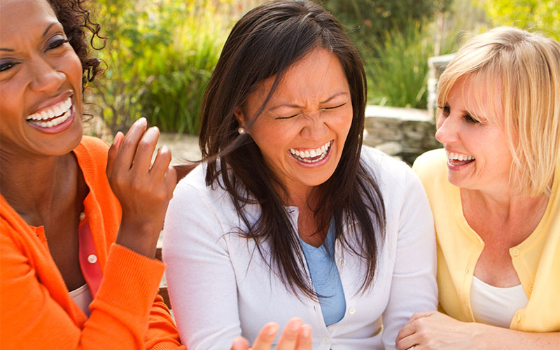 Diverse group of three middle-aged women laughing together.