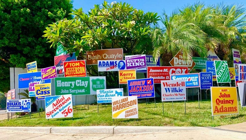 A residential front yard with 59 election style signs with the names of past individuals who has unsuccessful runs to be President of the United State of America.