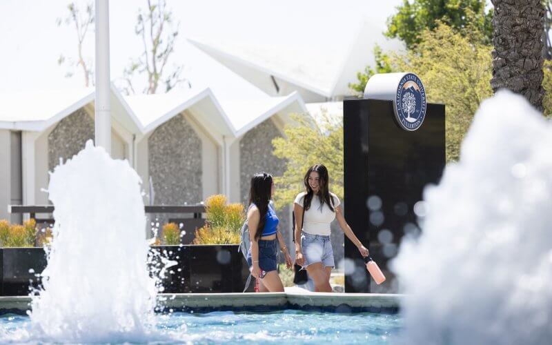 Two smiling students walk past fountain