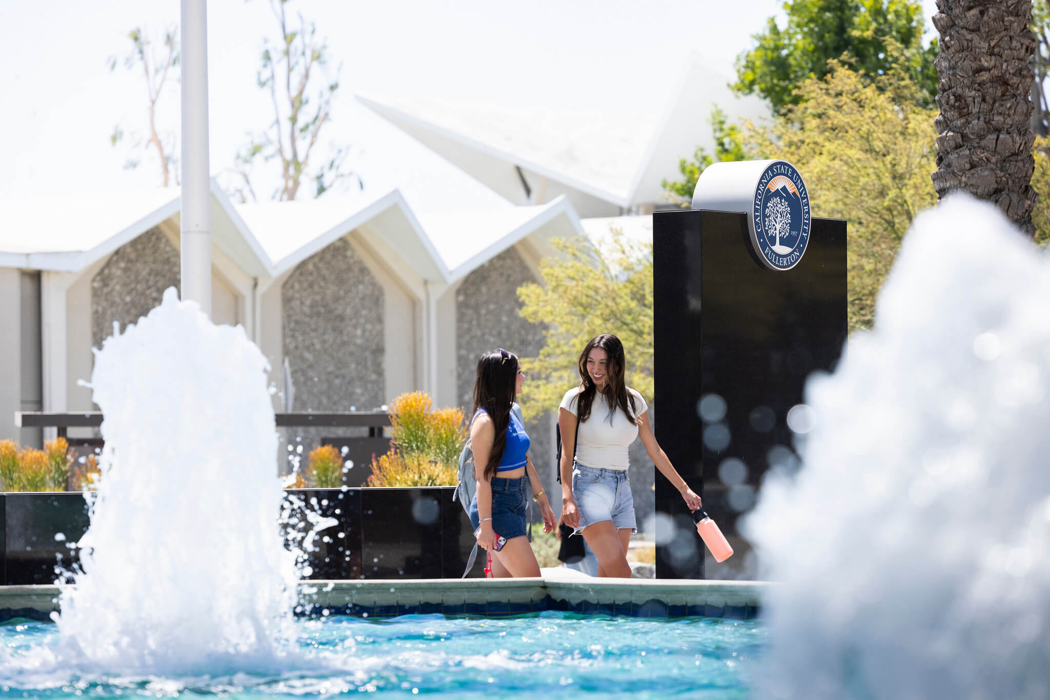 Two smiling students walk past fountain