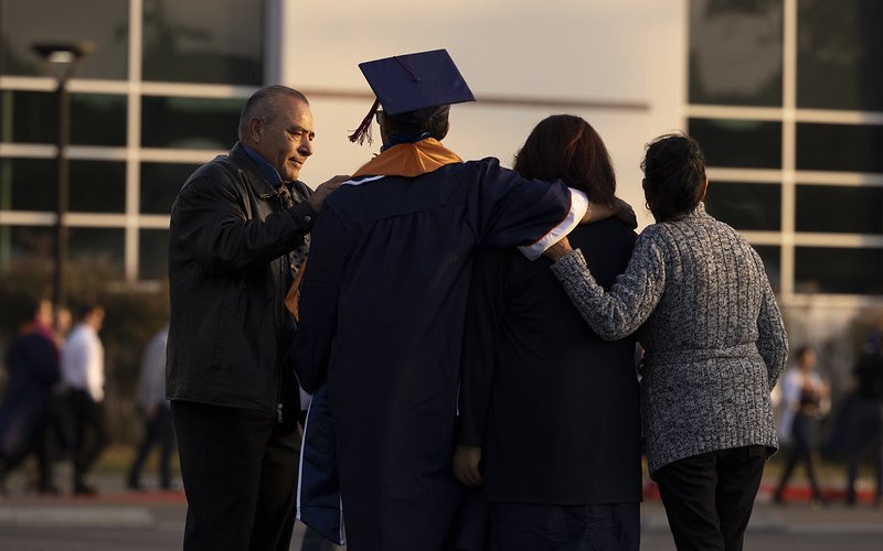 Family embracing Titan graduate dressed in regalia facing the Student Rec Center