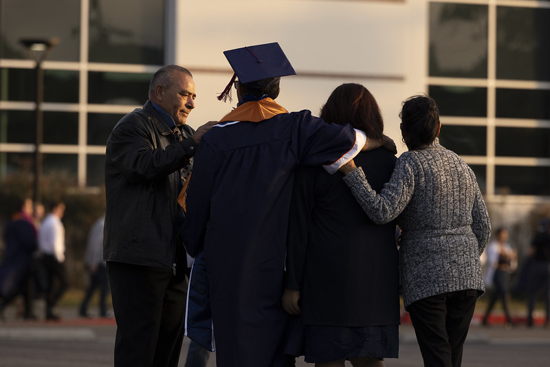 Family embracing Titan graduate dressed in regalia facing the Student Rec Center