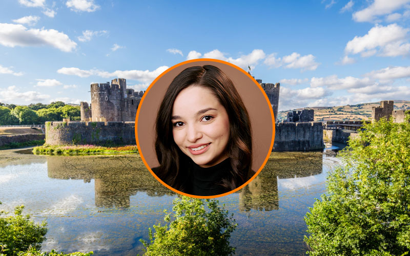 Circular image frame outlined in orange with a headshot of Rebecca Jauregui. Behind the frame is a background image of a historic castle in Wales.