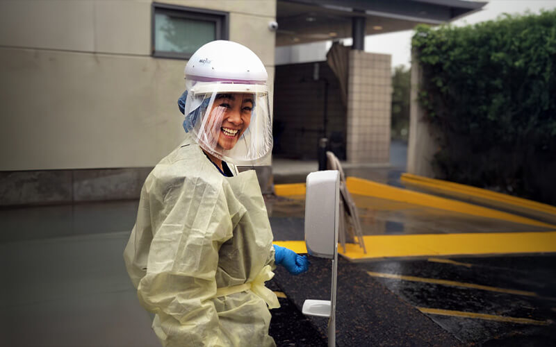 Smiling healthcare worker in protective gear near a medical facility.