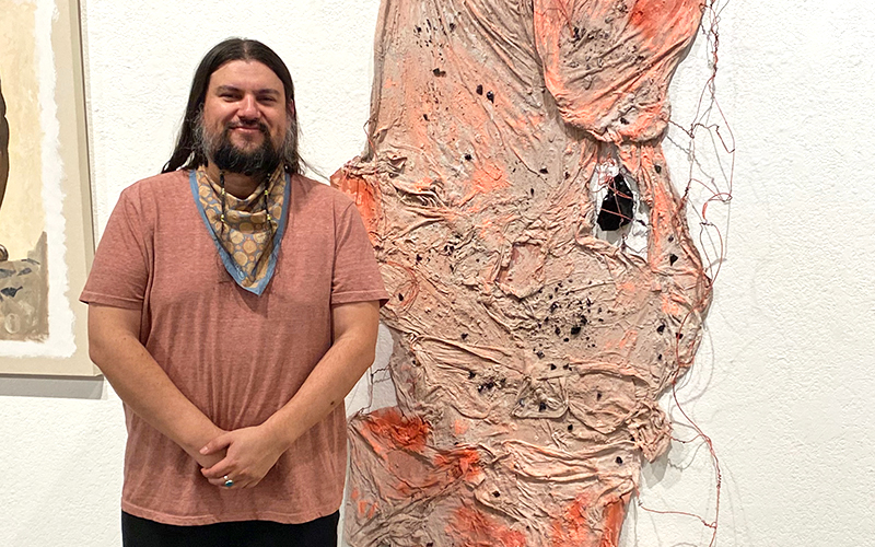 Juan Gomez standing in front of artwork on a wall