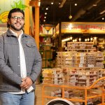 Man standing in a grocery store with a cart full of packaged goods.