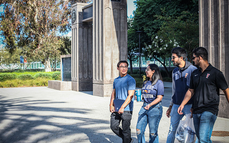 Four students wearing Titan gear walking past the archway on the CSUF campus.