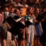 Students singing during a performance in CSUF's Meng Hall holding black binders