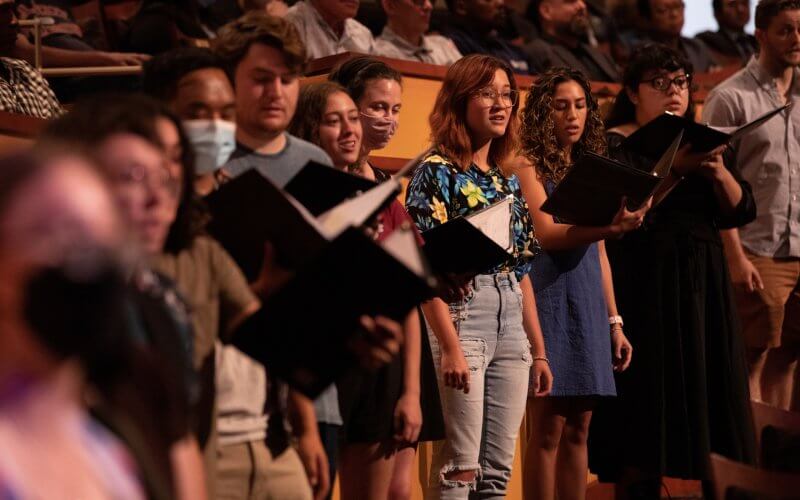 Students singing during a performance in CSUF's Meng Hall holding black binders