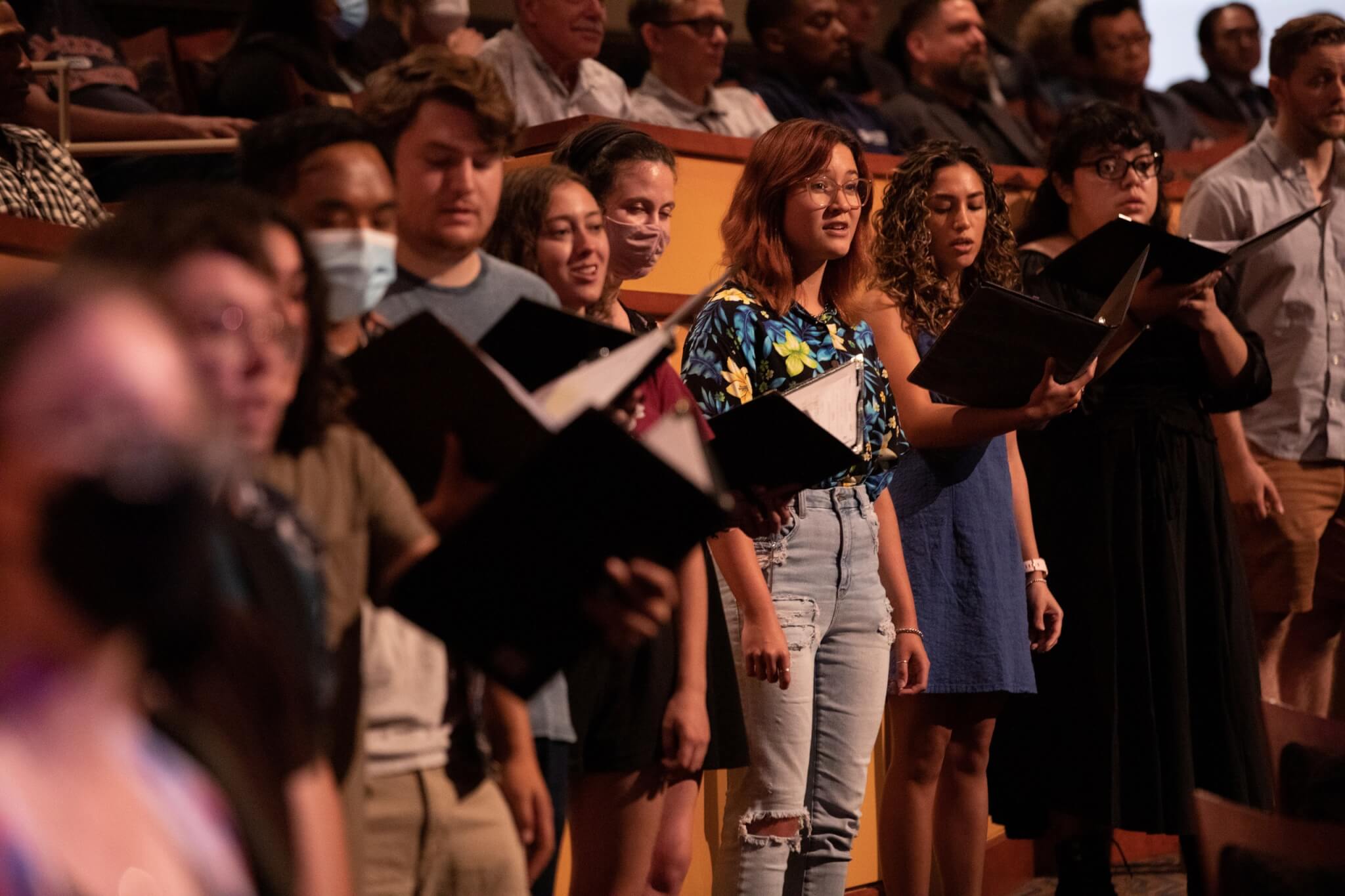 Students singing during a performance in CSUF's Meng Hall holding black binders