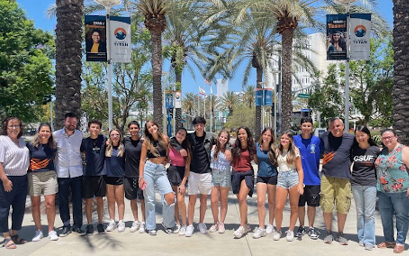 The group of high school students from For All English School in Brazil pose in a line for a photo at College Park on a sunny day.