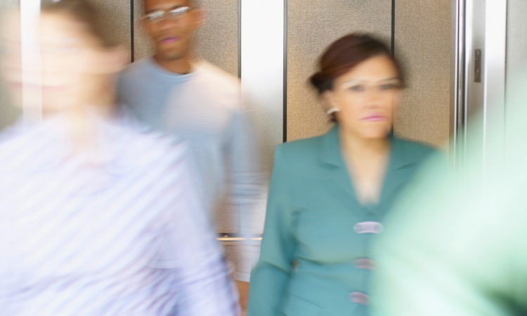 Multiple people in business attire walking out of an elevator with a slight blur implying they're moving fast.