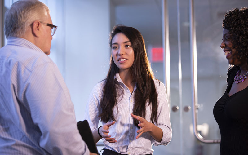 Young woman in business professional attire speaking with a middle aged man ad women in business professional attire.