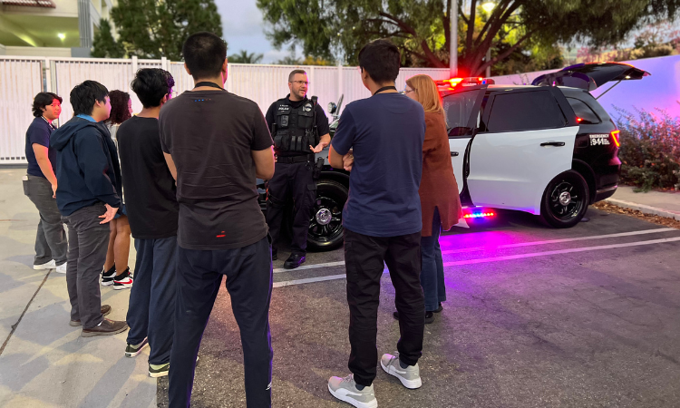 CSUF police officer standing around a police vehicle with community members discussing patrol operations.