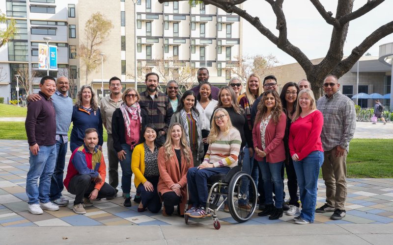 A group of adults smile in front of the residence halls at CSUF