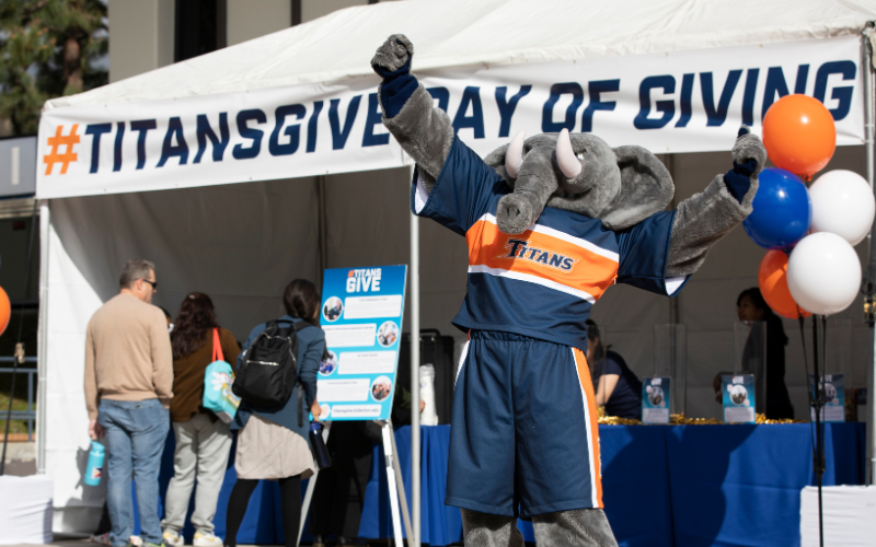 Tuffy standing in front of Titans Give Day of Giving tent raising an arm triumphantly in the air