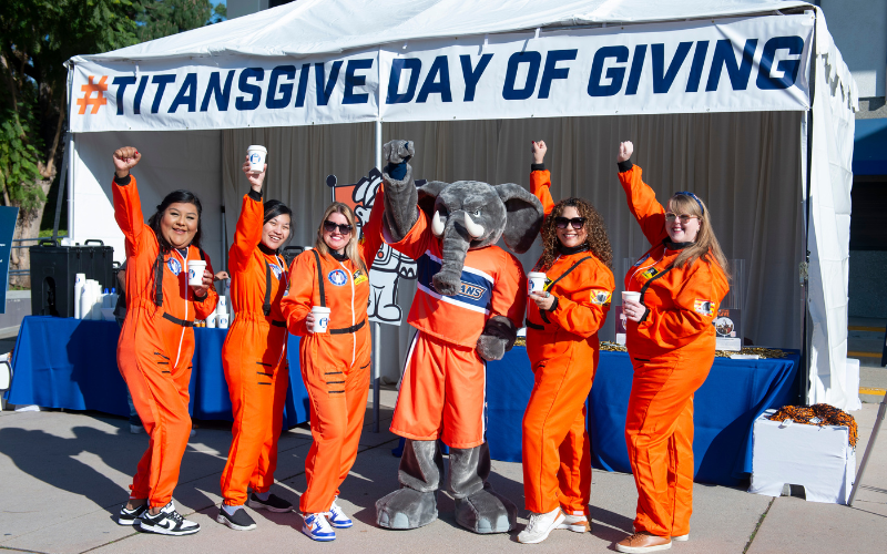 CSUF staff standing in front of Titans Give Day of Giving tent raising arms triumphantly in the air