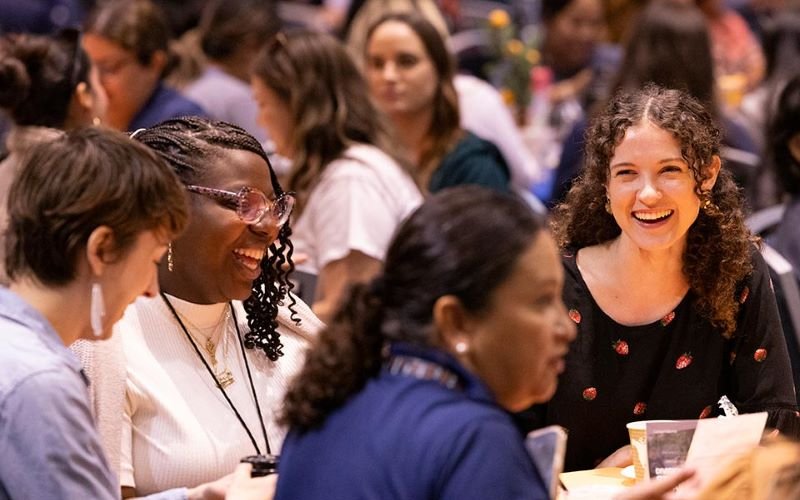 four female employees laugh at round table at a conference