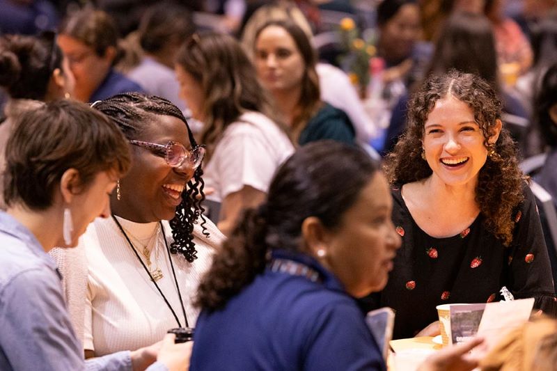 four female employees laugh at round table at a conference