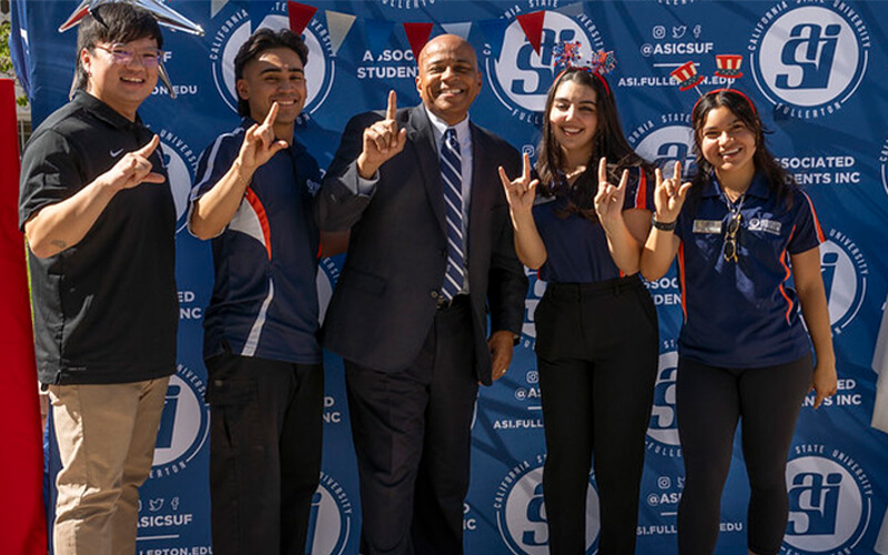 Associated Students Inc. leaders Gavon Ong, Joe Morales, Megan Hannoun and Suzette Morales smile and pose with CSUF President Ronald S. Rochon in front of an ASI backdrop.