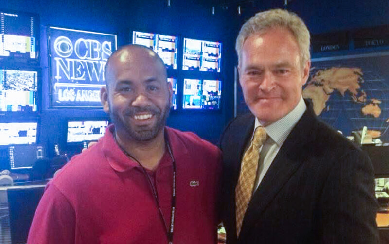 CSUF alum George Whipple Jr. and CBS correspondent Scott Pelly stand and smile in the CBS newsroom.