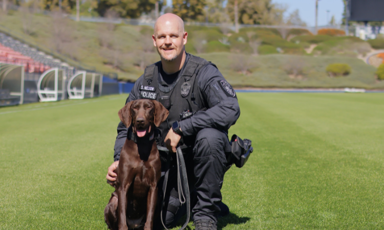 Cpl. Steve Nelson kneeling down next to K9 Liza, a German shorthaired pointer.