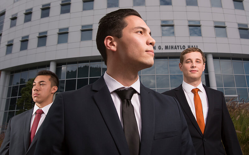 Three students in suits stand outside the College of Business and Economics