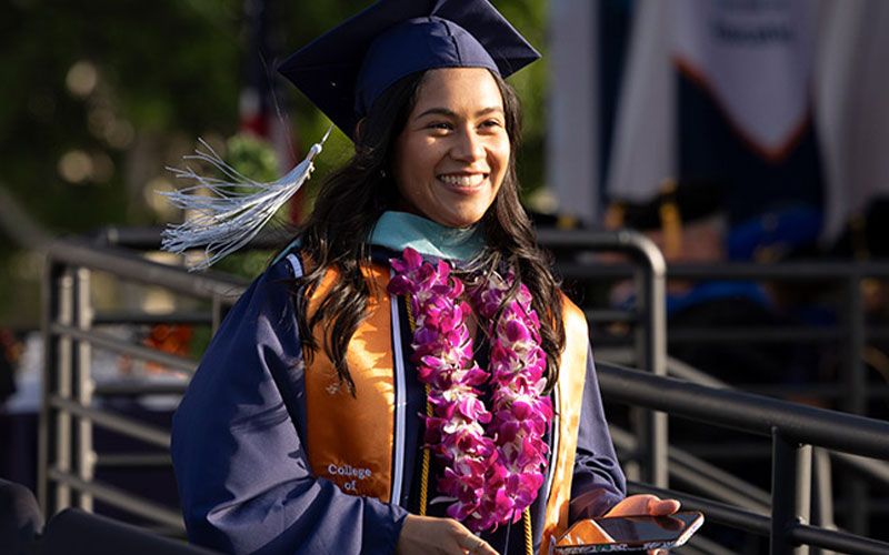 A Cal State Fullerton graduate wearing commencement regalia and an orchid lei.