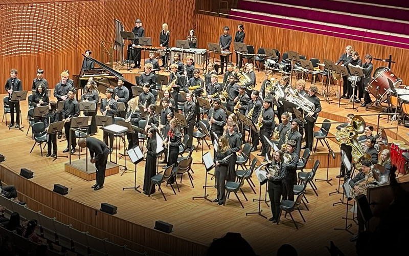 Conductor and musicians take a bow on stage in a concert hall.