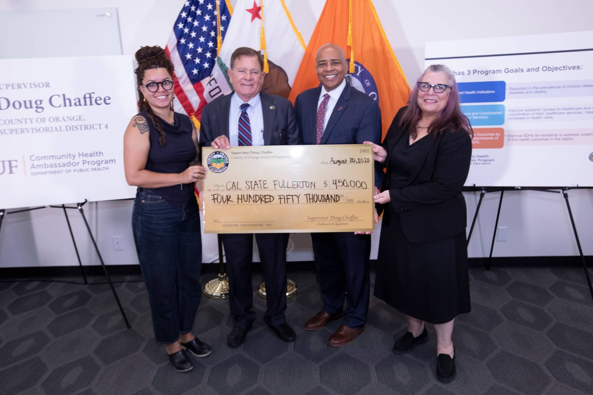 Cal State Fullerton officials and Orange County Board of Supervisors Chair Doug Chaffee pose with a giant check in front of County of Orange flags and signage