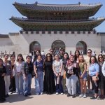 A group of college students stand in front of a Korean temple.