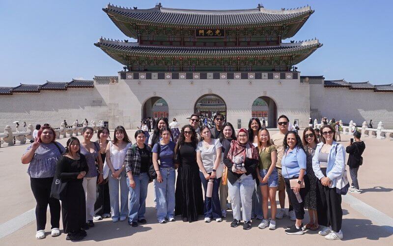 A group of college students stand in front of a Korean temple.