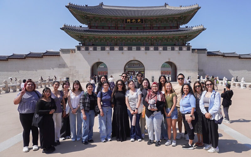 A group of college students stand in front of a Korean temple.
