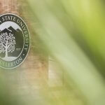 California State University, Fullerton emblem on a wall, partially obscured by green foliage in the foreground.