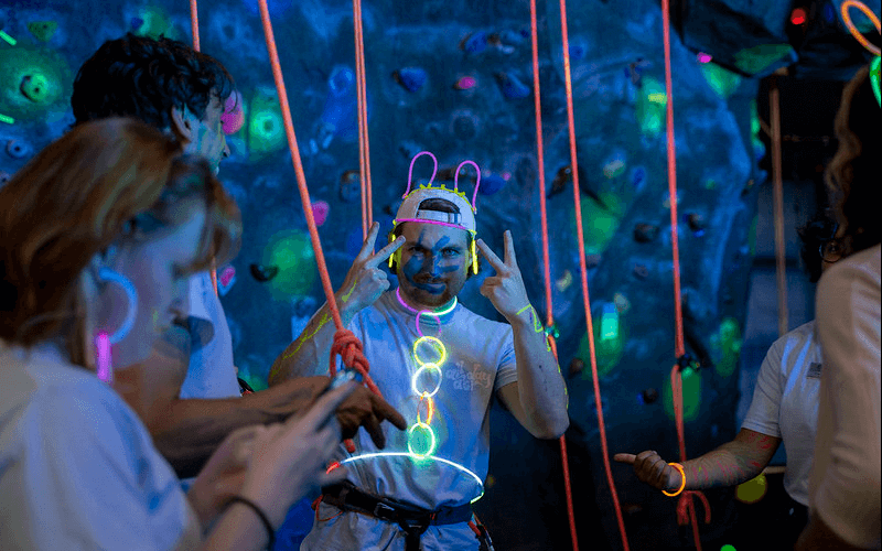 A CSUF student wearing glow-in-the-dark paint and accessories gets ready to climb the rock wall in the Student Recreation Center.